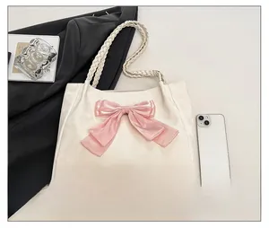 Detail of cream tote bag featuring a pink bow decoration and woven top handles