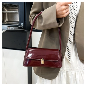 Side view of a vintage burgundy patent leather underarm bag worn by a model in a modern room