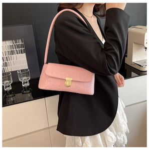 Detailed view of pink crocodile pattern leather shoulder bag with gold metal clasp on model