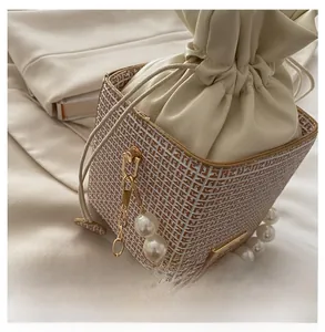 Detailed close-up of cream bucket bag with pearl handle and woven leather base detail