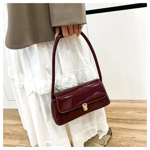 Close-up of wine red patent leather shoulder bag with metallic gold lock clasp