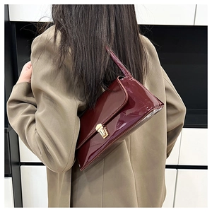 Detail of burgundy patent leather shoulder bag with gold metal buckle and sleek texture