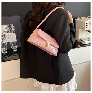 Fashionable pink crocodile pattern baguette bag worn over shoulder in minimalist studio