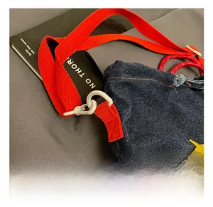 Detail of white swivel hook and red woven strap on blue denim crossbody bag