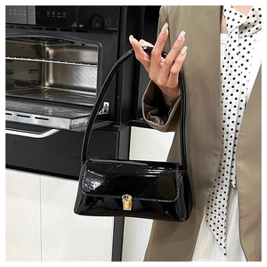 Close-up of black glossy patent leather bag with a gold metal square buckle and flap design