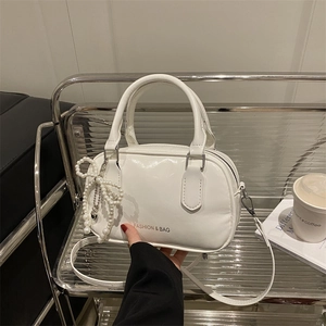 Chic white patent leather bowling bag with pearl bow charm on minimalist display