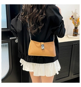 Détail du sac à bandoulière en cuir tressé caramel avec chaîne argentée porté par un mannequin