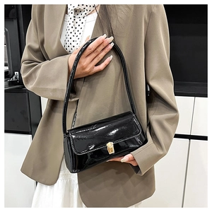 Detail of minimalist black patent leather shoulder bag with a gold metal clasp buckle