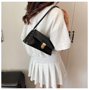 Detail of crocodile pattern leather shoulder bag with golden lock on female model