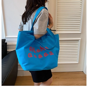Detail of blue canvas tote bag with red Aloha print shown on a shoulder in a room