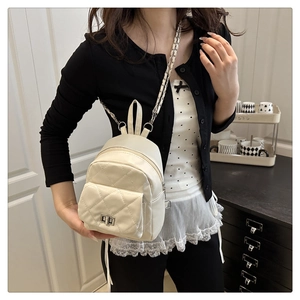 Close-up of white quilted mini backpack with silver metal twist lock and chain strap