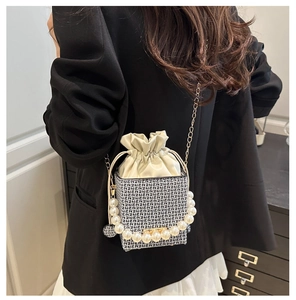 Close-up of woven bucket bag with pearl handle, gold chain strap and drawstring detail