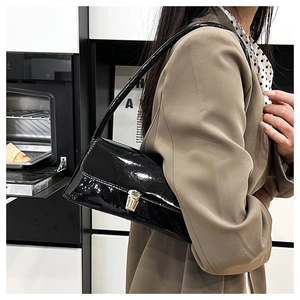 Close-up of black glossy patent leather shoulder bag with golden metallic twist lock