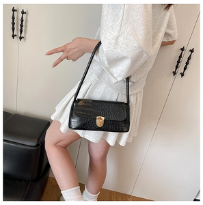 Detail of black crocodile texture handbag with golden metal clasp worn by a model