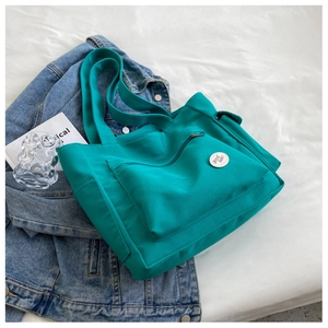 Close-up of turquoise canvas tote bag featuring a front zipper pocket and round graphic