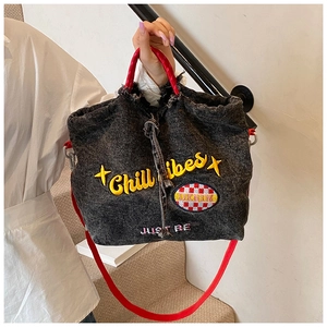 Detail of washed denim tote showing Chill Vibes embroidery and red plaid patch texture