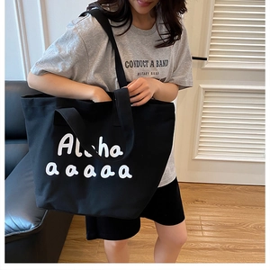 Detailed view of black canvas tote bag with white Aloha print worn by model