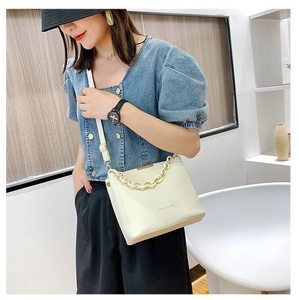 Close-up of cream bucket bag with decorative chunky gold chain strap and PU leather finish