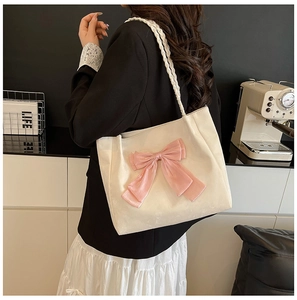 Close-up of white tote bag featuring a pink bow and woven shoulder strap on a model
