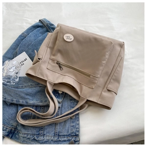 Detail of khaki oxford tote bag with front zipper pocket and decorative logo patch