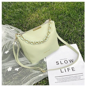 Detail of light green bucket bag with mixed acrylic and metal chain handle on grass