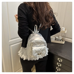 Detail of silver quilted mini backpack with metallic finish and chain straps on model