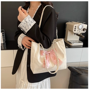 Detail of cream tote bag featuring a pink silk bow and woven straps in a chic cafe setting