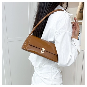 Detail of glossy brown patent leather baguette bag with elegant gold metal buckle