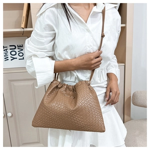 Borsa a secchiello intrecciata marrone indossata da modella con logo dorato e lacci