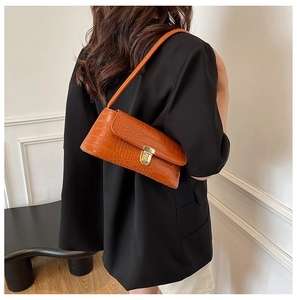 Detail view of orange crocodile texture shoulder bag with golden metal buckle clasp