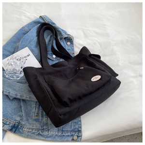 Close-up of black oxford tote bag with front zipper pocket and decorative Good Luck patch