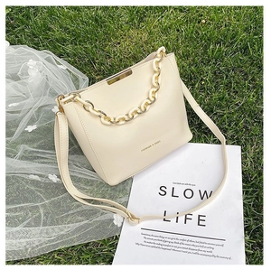 Detail view of beige crossbody bucket bag with thick plastic chain and gold metal trim