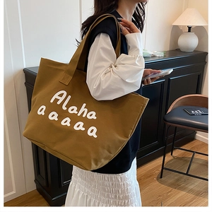 Detail of a large brown canvas tote bag with white Alaha lettering in a lifestyle setting