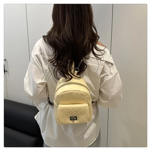 Detail of a creamy yellow quilted backpack with metal twist lock and stitching