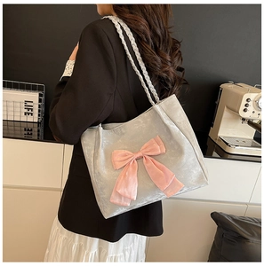 Close-up of a silver velvet tote bag with a pink satin bow and braided strap details