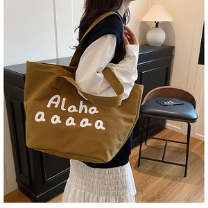Brown canvas tote bag with white letter print worn over the shoulder in a home setting