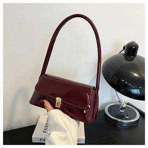 Detailed close-up of glossy burgundy patent leather shoulder bag with gold metal buckle