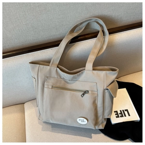 Detail of beige canvas tote bag showing zipper pocket and side flap compartment