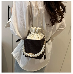 Detail of dark brown woven bucket bag with pearl handle and cream drawstring insert