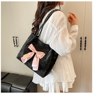 Detail of a black velvet tote bag featuring a large pink satin bow and woven rope handles
