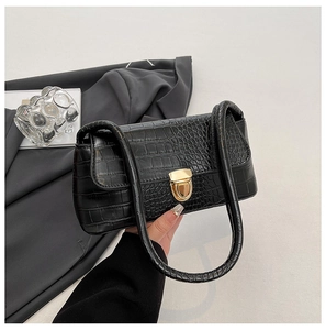 Detail of black crocodile texture handbag with golden metallic clasp and smooth leather handle