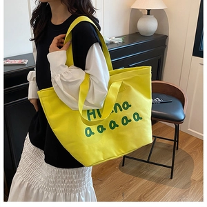 Detail of yellow canvas tote bag with green letters and dual shoulder straps