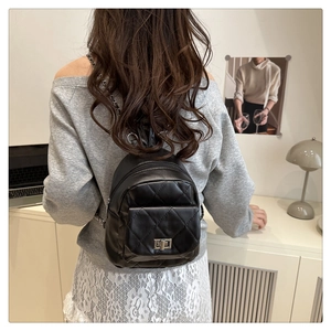Detail of a black quilted mini backpack with chain straps shown on a model's back