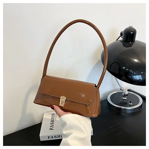 Detail of glossy brown patent leather baguette bag with long handle and gold buckle