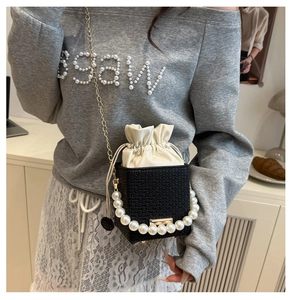 Detail of a black woven bucket bag featuring elegant pearl handle and gold chain strap