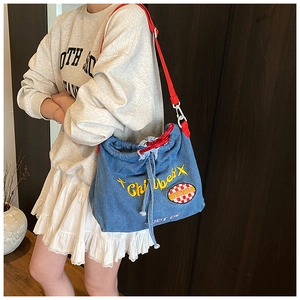Detail of blue denim bucket bag featuring yellow embroidery and red drawstring closure