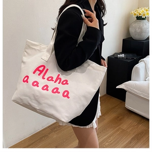 Lifestyle view of a large white canvas tote bag with pink lettering on a female model