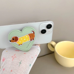 Close-up of leather heart-shaped phone grip featuring an embroidered dachshund puppy