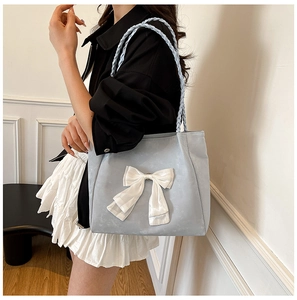 Detail of light blue tote bag with a large white bow and woven shoulder straps