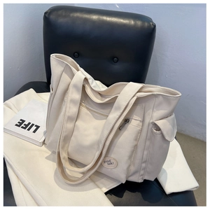 Detail of a creamy white canvas tote bag featuring front zipper pockets and lucky embroidery